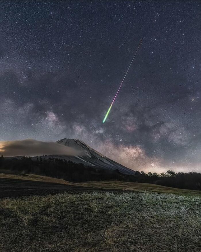 Meteor streaks across a starry sky over a mountain, showcasing stunning space photography.