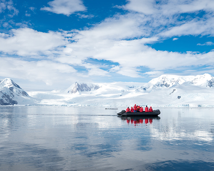 Team in red jackets exploring remote Antarctica waters in a black boat under a bright blue sky. Team in red jackets exploring remote Antarctica waters in a black boat under a bright blue sky.