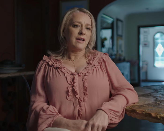 Woman in a pink blouse sitting at a table, discussing a scandal involving a disgraced actor. Woman in a pink blouse sitting at a table, discussing a scandal involving a disgraced actor.