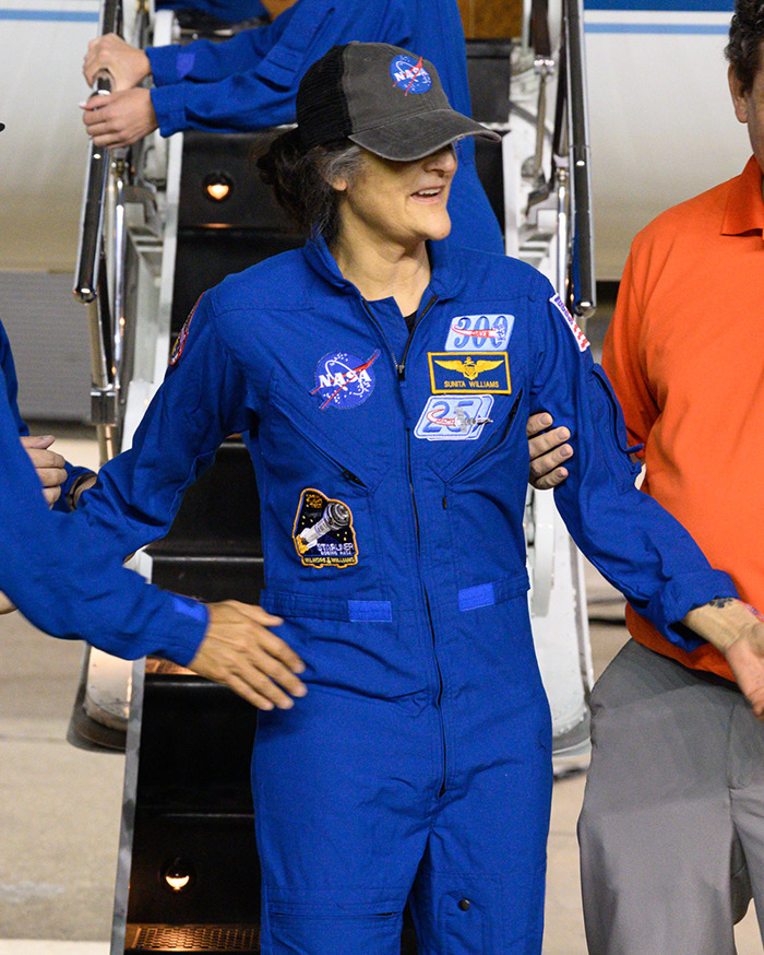 NASA astronaut in blue suit and cap, being assisted while exiting a spacecraft. NASA astronaut in blue suit and cap, being assisted while exiting a spacecraft.