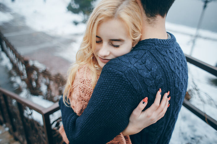 Couple embracing warmly in a snowy setting, wearing knitted sweaters.