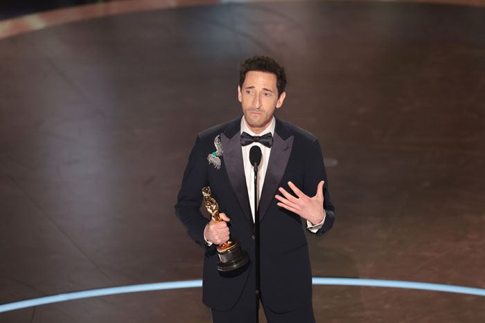 A man in a tuxedo holding an Oscar statue on stage, 2025. A man in a tuxedo holding an Oscar statue on stage, 2025.