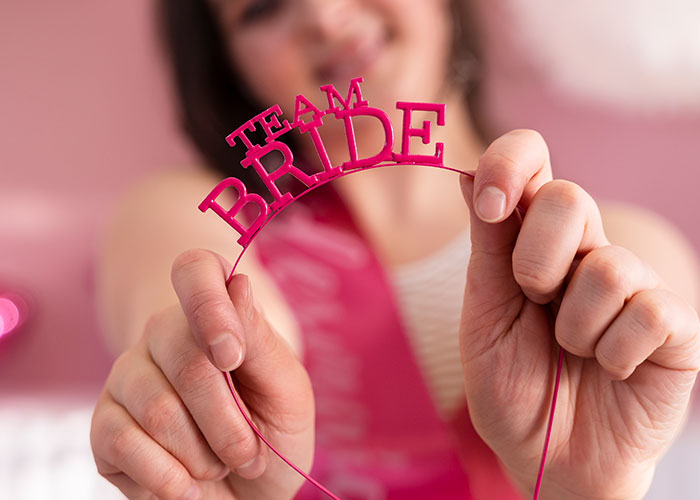 Person holding a pink "Team Bride" headband with a blurred background, emphasizing wedding theme. Person holding a pink "Team Bride" headband with a blurred background, emphasizing wedding theme.
