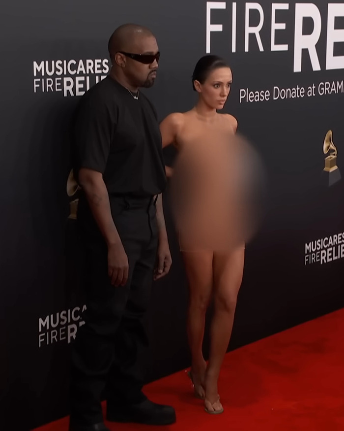 Kanye West in black attire and sunglasses with Bianca Censori in blurred outfit on Grammys red carpet. Kanye West in black attire and sunglasses with Bianca Censori in blurred outfit on Grammys red carpet.