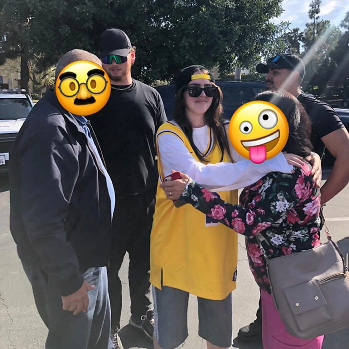 Billie Eilish look-alike in a yellow jersey takes photos with fans at a crowded outdoor event. Billie Eilish look-alike in a yellow jersey takes photos with fans at a crowded outdoor event.