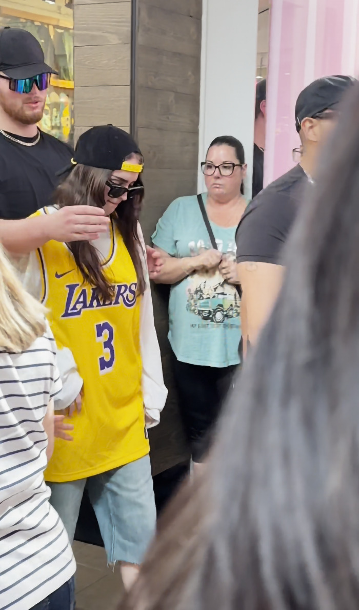 Billie Eilish look-alike in yellow Lakers jersey surrounded by people at a busy mall event. Billie Eilish look-alike in yellow Lakers jersey surrounded by people at a busy mall event.