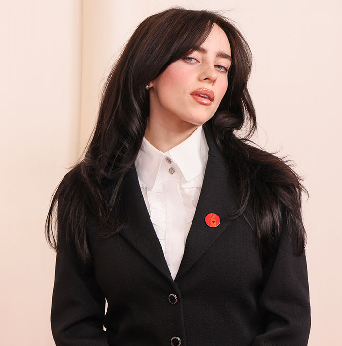 Billie Eilish in a formal outfit with a red pin, posing for a portrait. Billie Eilish in a formal outfit with a red pin, posing for a portrait.