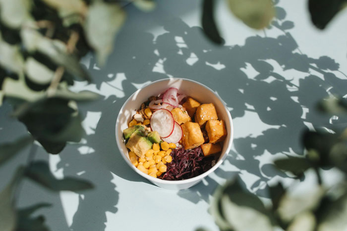A colorful salad bowl with corn, radishes, and greens, surrounded by leafy shadows, related to cooking. A colorful salad bowl with corn, radishes, and greens, surrounded by leafy shadows, related to cooking.