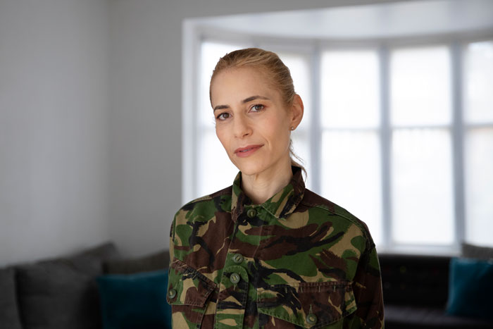 Woman in a camo jacket stands in a living room, expressing emotions related to motherhood fears. Woman in a camo jacket stands in a living room, expressing emotions related to motherhood fears.