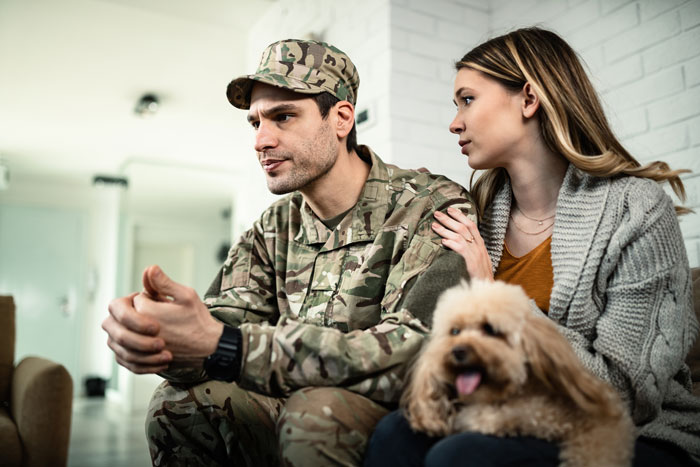 Couple discussing motherhood, man in military uniform, woman concerned, comforting dog nearby. Couple discussing motherhood, man in military uniform, woman concerned, comforting dog nearby.