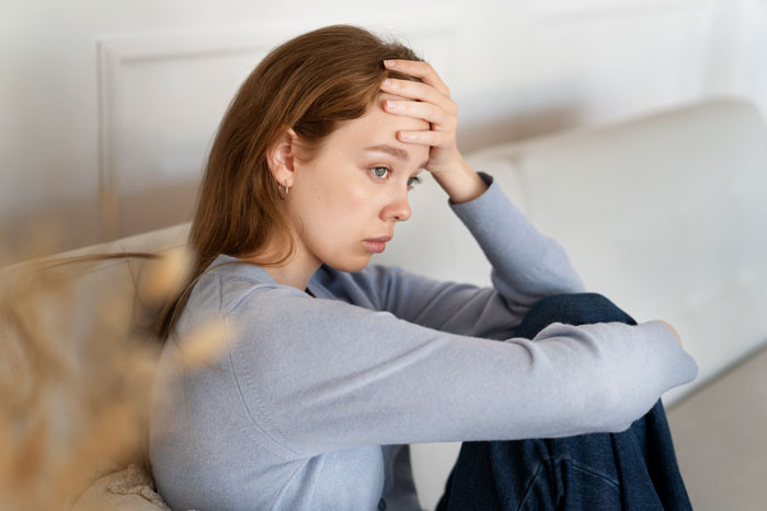 Woman looking anxious on a couch, hand on forehead, representing fear of motherhood. Woman looking anxious on a couch, hand on forehead, representing fear of motherhood.
