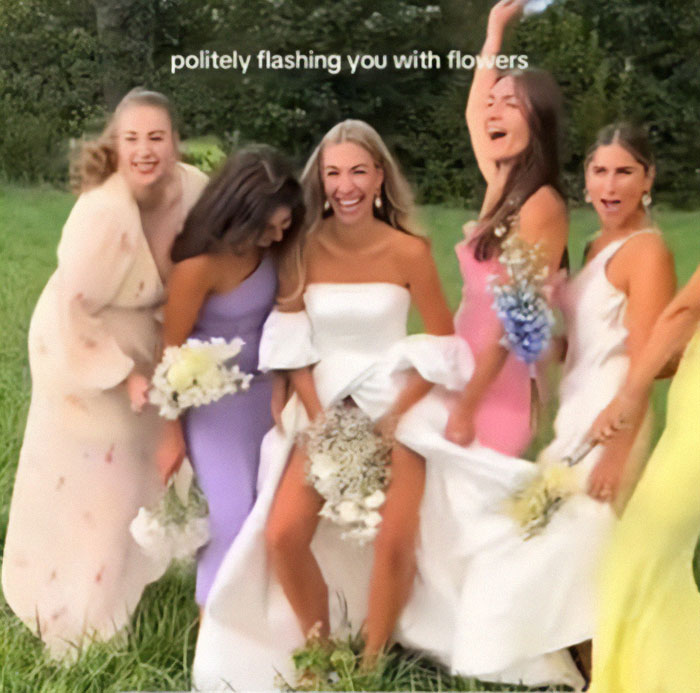 Bride flashes underwear during wedding photoshoot with bridesmaids holding flowers, laughing in a grassy field. Bride flashes underwear during wedding photoshoot with bridesmaids holding flowers, laughing in a grassy field.