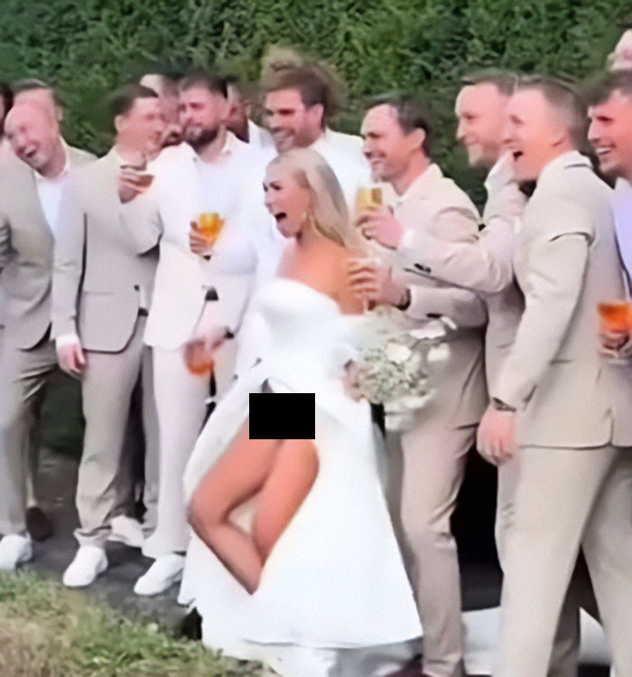 Bride flashes underwear during photoshoot with groomsmen laughing, capturing a quirky wedding moment. Bride flashes underwear during photoshoot with groomsmen laughing, capturing a quirky wedding moment.