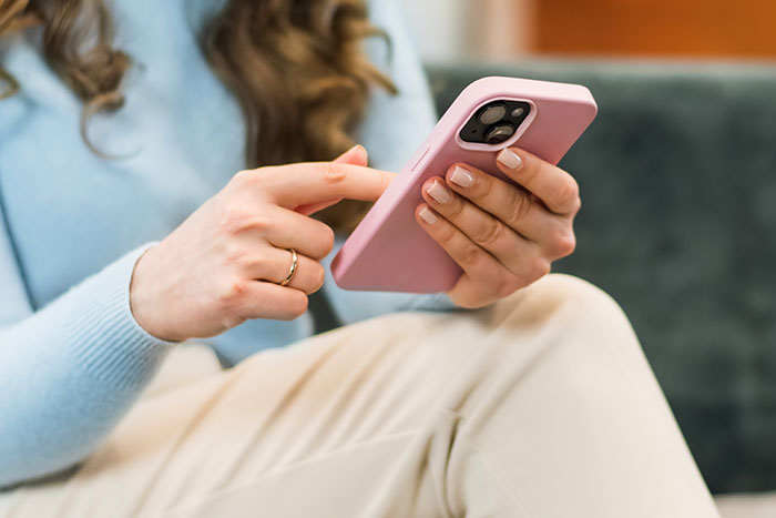 Woman using smartphone at home, wearing a blue top, focused on the screen, with an engagement ring on her finger. Woman using smartphone at home, wearing a blue top, focused on the screen, with an engagement ring on her finger.