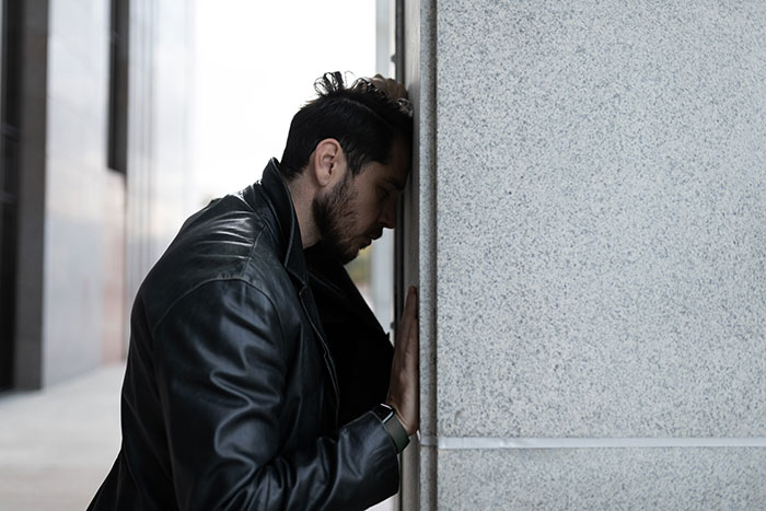 Man in leather jacket, leaning against a wall, looking contemplative about wedding guest choice. Man in leather jacket, leaning against a wall, looking contemplative about wedding guest choice.