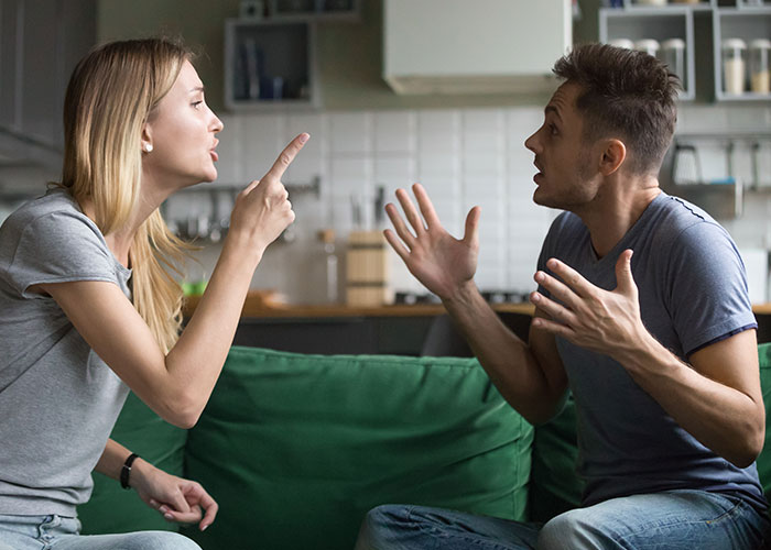 Man and woman arguing on the couch, emphasizing relationship tension with his choice of plus-one to the wedding. Man and woman arguing on the couch, emphasizing relationship tension with his choice of plus-one to the wedding.