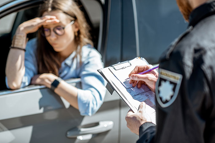 A woman in a car looks distressed as a police officer writes a ticket. A woman in a car looks distressed as a police officer writes a ticket.