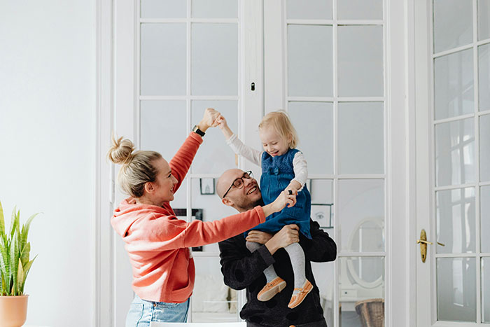A woman and man happily play with a young child in a bright room, symbolizing family togetherness. A woman and man happily play with a young child in a bright room, symbolizing family togetherness.