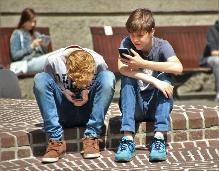 Two boys sitting on brick steps, focused on their phones, symbolizing disbelief over being bullied for trivial things.