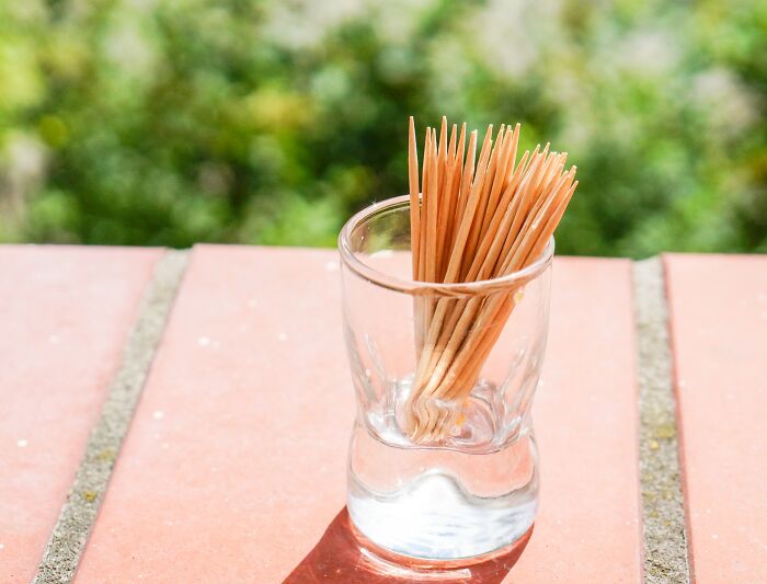 Glass with toothpicks on a red tile, symbolizing simple things people got bullied over, with greenery in the background.