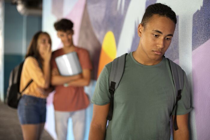 Teenager looking upset while peers whisper in the background, highlighting the impact of bullying.
