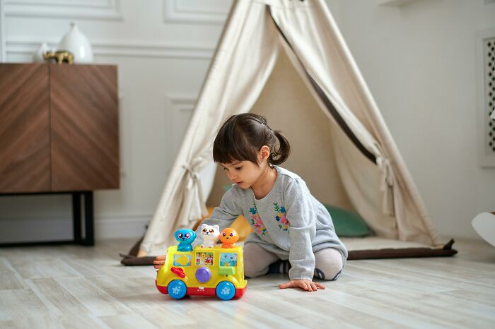 Child playing with colorful toy bus in cozy room with a teepee in the background, reflecting childhood innocence.