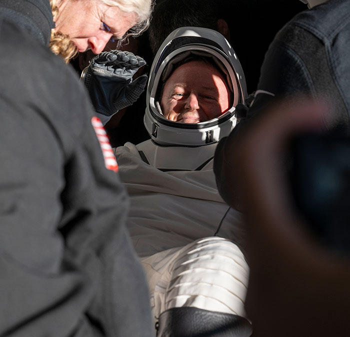 NASA astronaut in suit, smiling after Earth return, with concern for his health being addressed by the crew. NASA astronaut in suit, smiling after Earth return, with concern for his health being addressed by the crew.