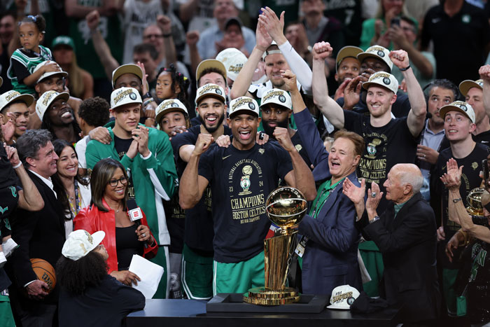 Boston Celtics players celebrating a championship win, wearing team gear and gathered around a trophy. Boston Celtics players celebrating a championship win, wearing team gear and gathered around a trophy.