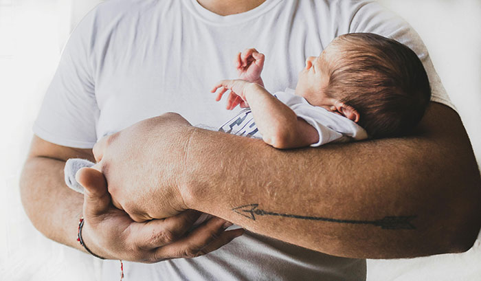Man in white shirt holding a newborn, with a tattooed arm. Man in white shirt holding a newborn, with a tattooed arm.