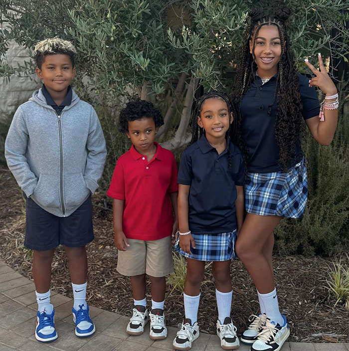 Children posing outdoors in casual and school attire, smiling in front of greenery. Children posing outdoors in casual and school attire, smiling in front of greenery.
