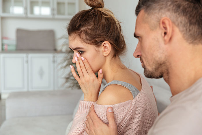 Man and woman on a couch, emotional moment as he discusses wanting kids, touching her shoulder gently. Man and woman on a couch, emotional moment as he discusses wanting kids, touching her shoulder gently.