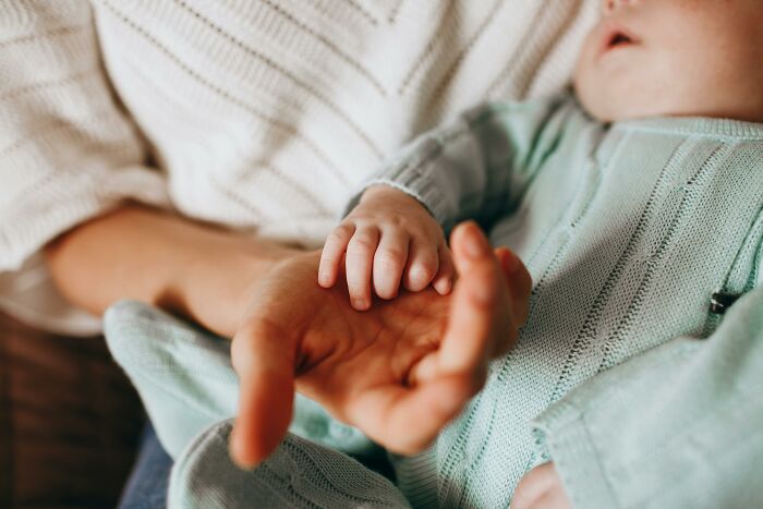 Adult hand holding a baby's hand, highlighting childfree group dynamics and baby drama themes. Adult hand holding a baby's hand, highlighting childfree group dynamics and baby drama themes.