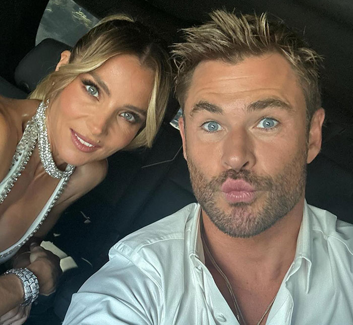Chris Hemsworth taking a playful selfie in a car, wearing a white shirt, alongside another person. Chris Hemsworth taking a playful selfie in a car, wearing a white shirt, alongside another person.