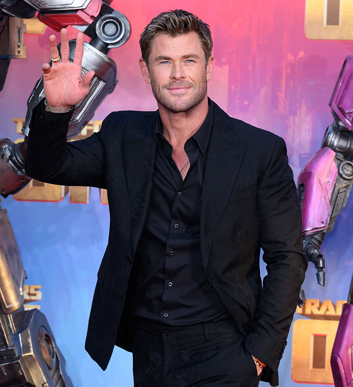 Chris Hemsworth smiling in a suit at an event, colorful background. Chris Hemsworth smiling in a suit at an event, colorful background.