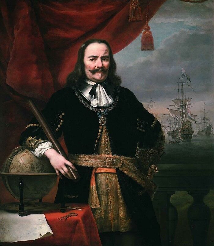 Portrait of a historical figure in lavish attire, holding a telescope beside a globe, with ships visible in the background.