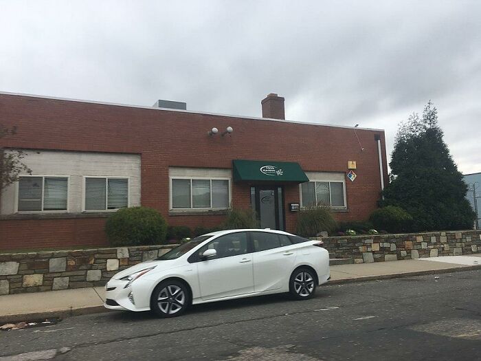 A white car parked in front of a brick building with a green awning, cloudy skies above, Napoleon theme suggested.