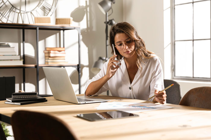 Woman working at a table with a phone and laptop, discussing wedding prep for bride. Woman working at a table with a phone and laptop, discussing wedding prep for bride.