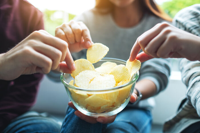 Hands reaching for chips in a bowl, highlighting misunderstood "healthy" snacks.