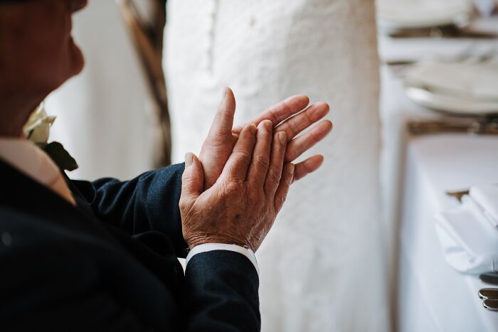 Person in formal attire clapping at a wedding ceremony, highlighting a normal societal tradition.