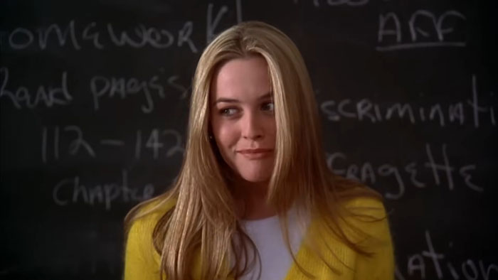 Blonde woman in yellow cardigan with blackboard background, evoking Clueless nostalgia. Blonde woman in yellow cardigan with blackboard background, evoking Clueless nostalgia.