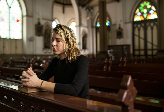 Woman in deep thought sitting in a church pew, representing the insignificance of being stuck forever in contemplation.