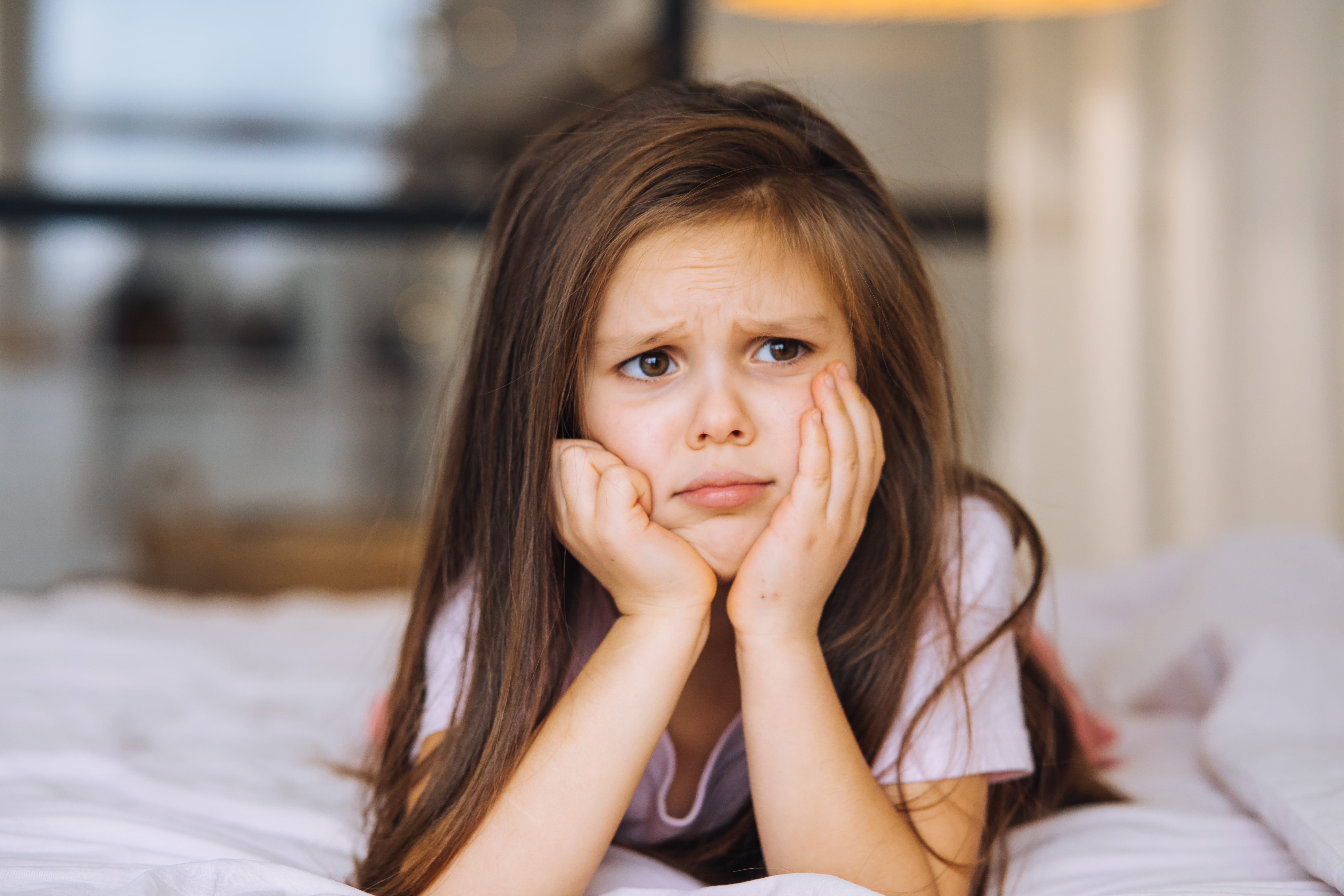 A young girl looking sad, resting her face in her hands, symbolizing exclusion from parties and events. A young girl looking sad, resting her face in her hands, symbolizing exclusion from parties and events.