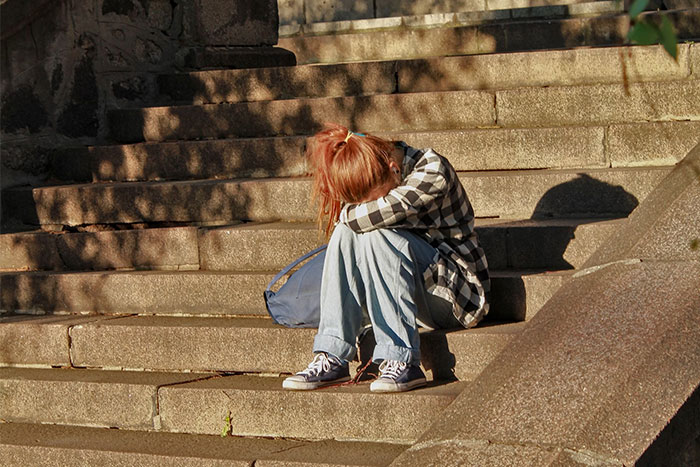 A young girl sitting alone on stone steps, wearing casual clothes, with her head down. A young girl sitting alone on stone steps, wearing casual clothes, with her head down.
