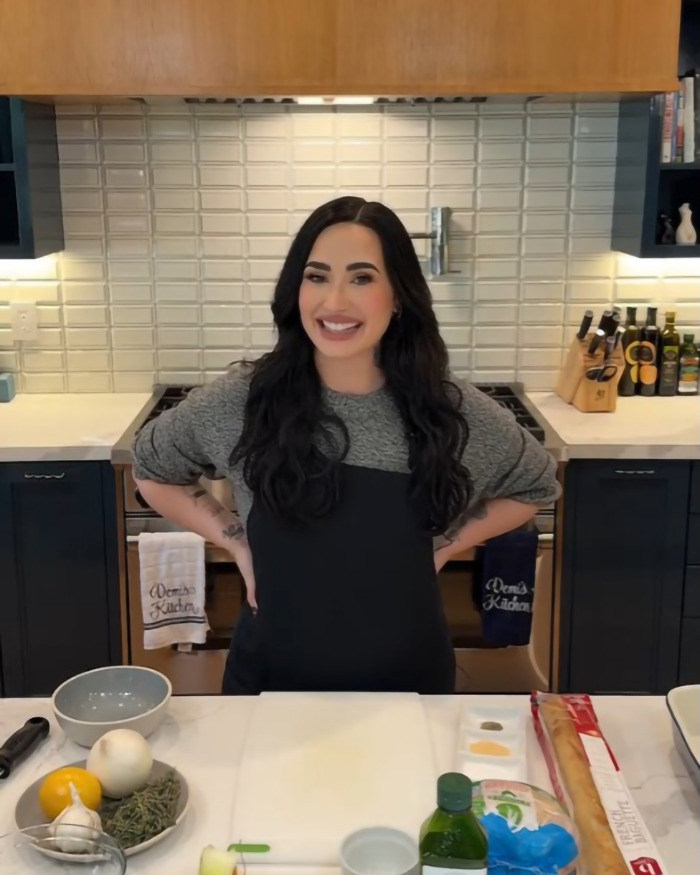 Demi Lovato smiling in a kitchen, wearing a black apron, showcasing weight loss transformation. Demi Lovato smiling in a kitchen, wearing a black apron, showcasing weight loss transformation.