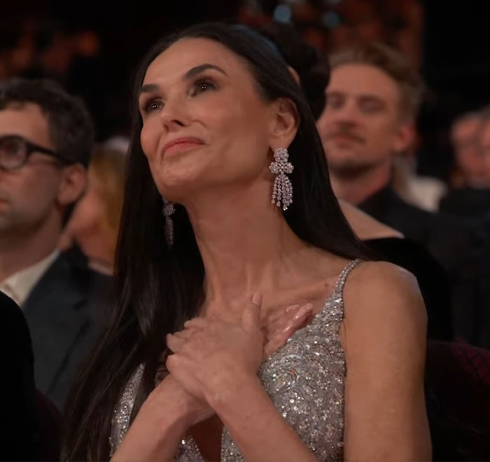 Demi Moore at the Oscars, hands on chest, showing emotion during a heartfelt moment. Demi Moore at the Oscars, hands on chest, showing emotion during a heartfelt moment.