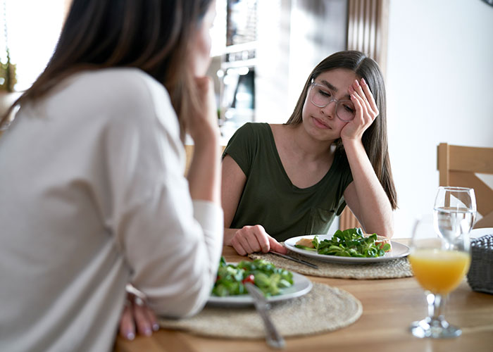 Teen girl looking frustrated at dinner with step-mom, learning a life lesson about her mom. Teen girl looking frustrated at dinner with step-mom, learning a life lesson about her mom.