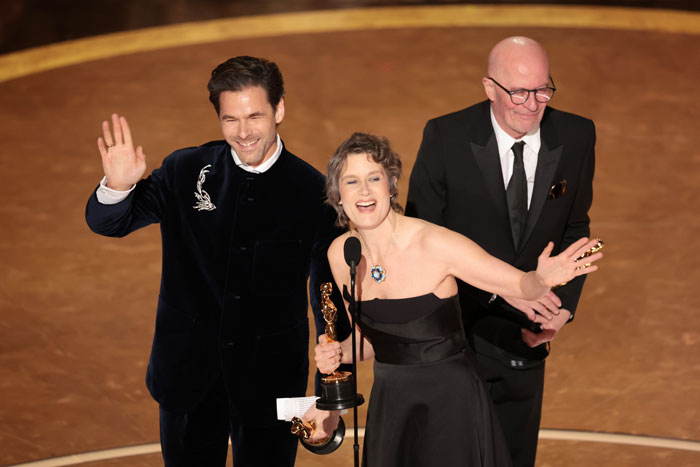 People celebrating on stage at the Oscars 2025, holding an award and waving to the audience. People celebrating on stage at the Oscars 2025, holding an award and waving to the audience.