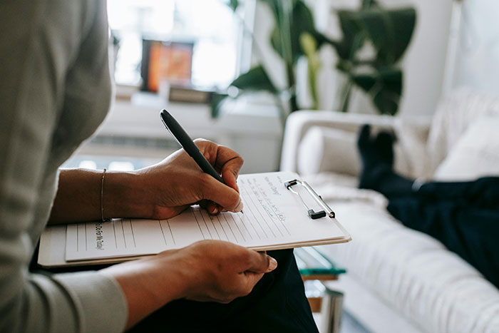 Person writing on a clipboard in a living room, possibly discussing financial behavior consequences. Person writing on a clipboard in a living room, possibly discussing financial behavior consequences.