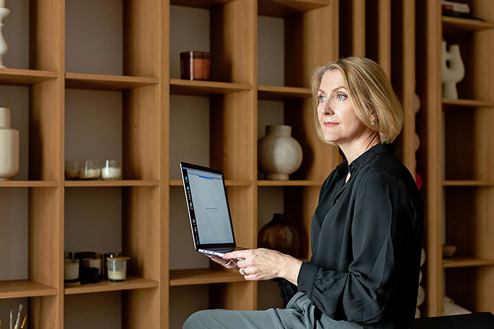 Woman holding a laptop in a modern office, shelves in background, expressing concern over university funds issue. Woman holding a laptop in a modern office, shelves in background, expressing concern over university funds issue.