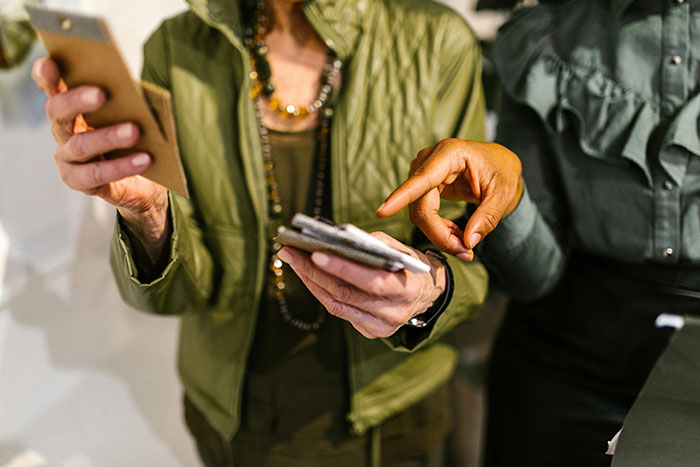 Two women in stylish outfits discussing an influencer trip on their smartphones. Two women in stylish outfits discussing an influencer trip on their smartphones.